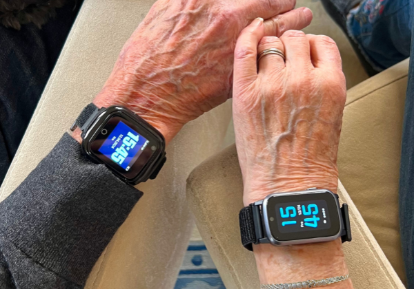 Två seniorer håller hand och båda bär Sensorems trygghetslarm. En av smartklockorna är av smal modell.